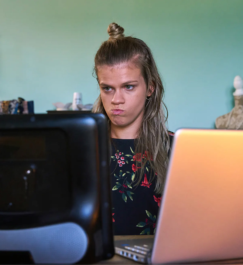 Photo of a young woman focused with concentration looking at her AAC device and laptop computer.